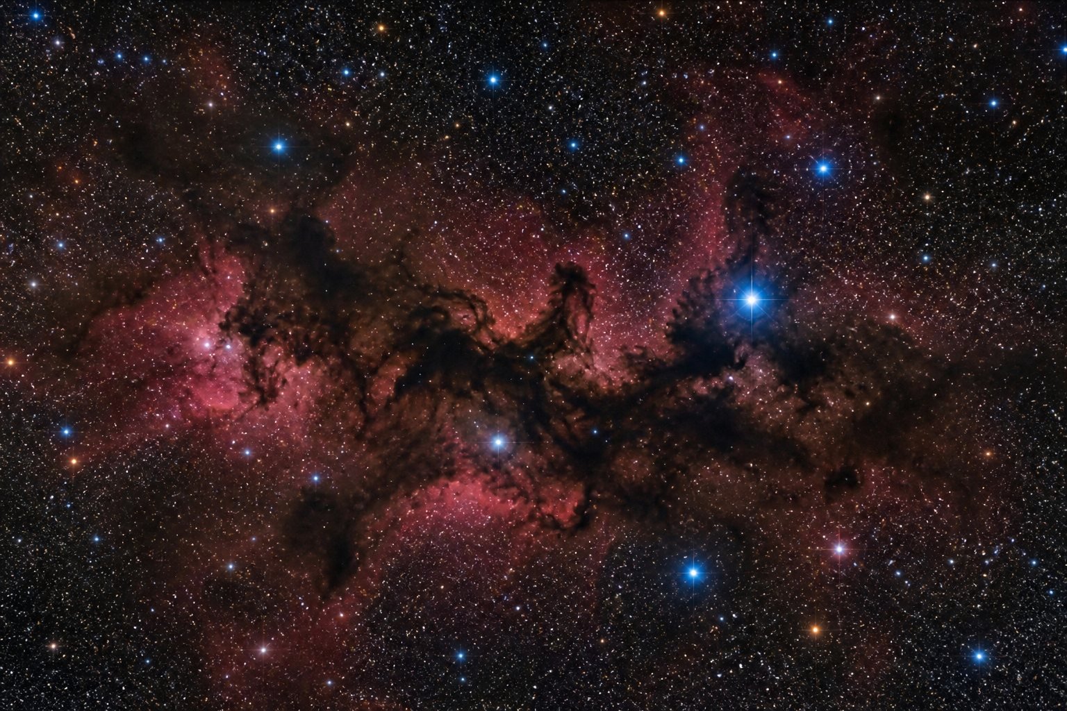 Deep-space photo: red emission nebula with dark dust lanes and blue stars